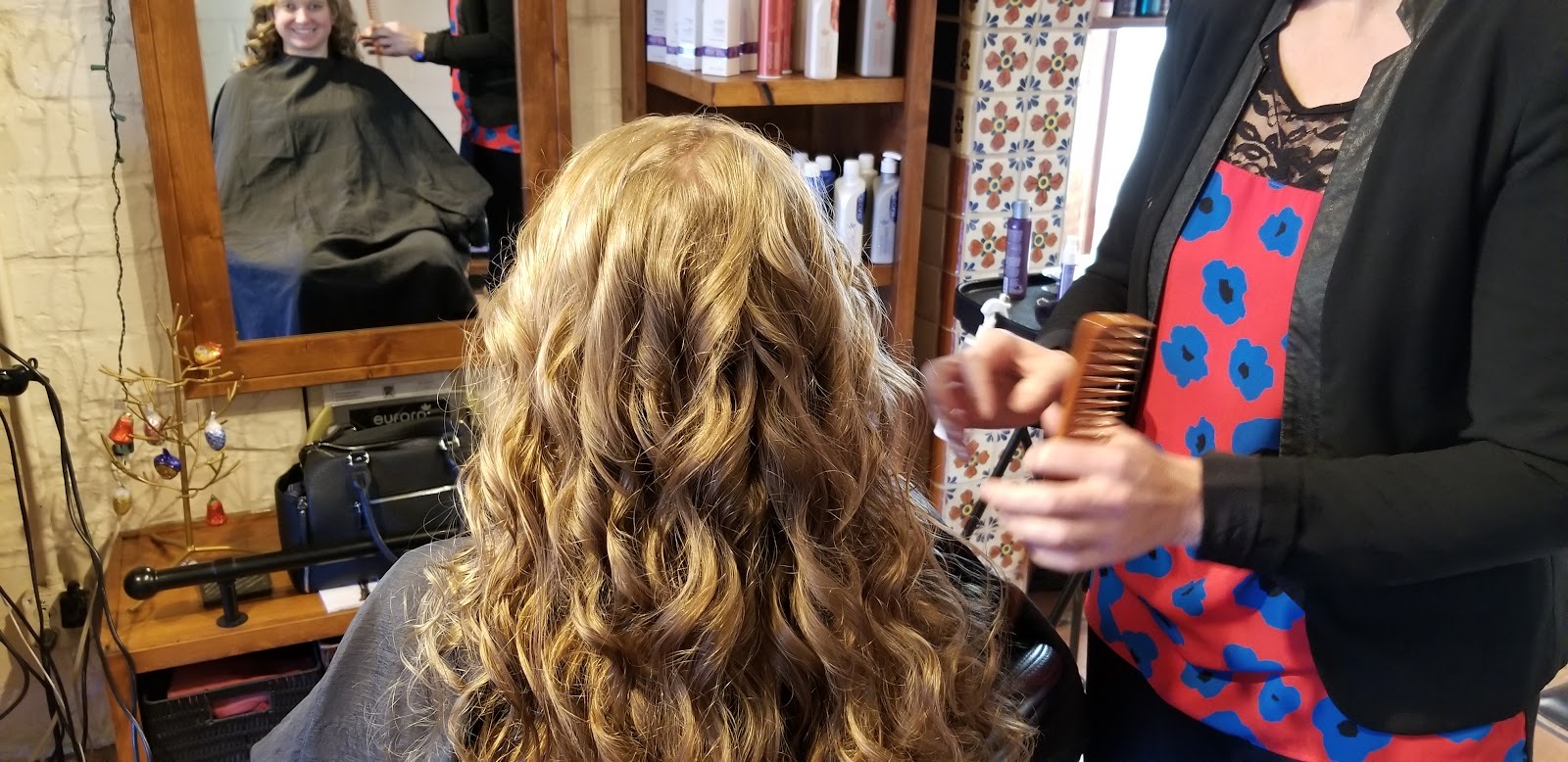 A stylist combing out a guest’s long, freshly styled curls at Gloss Studio