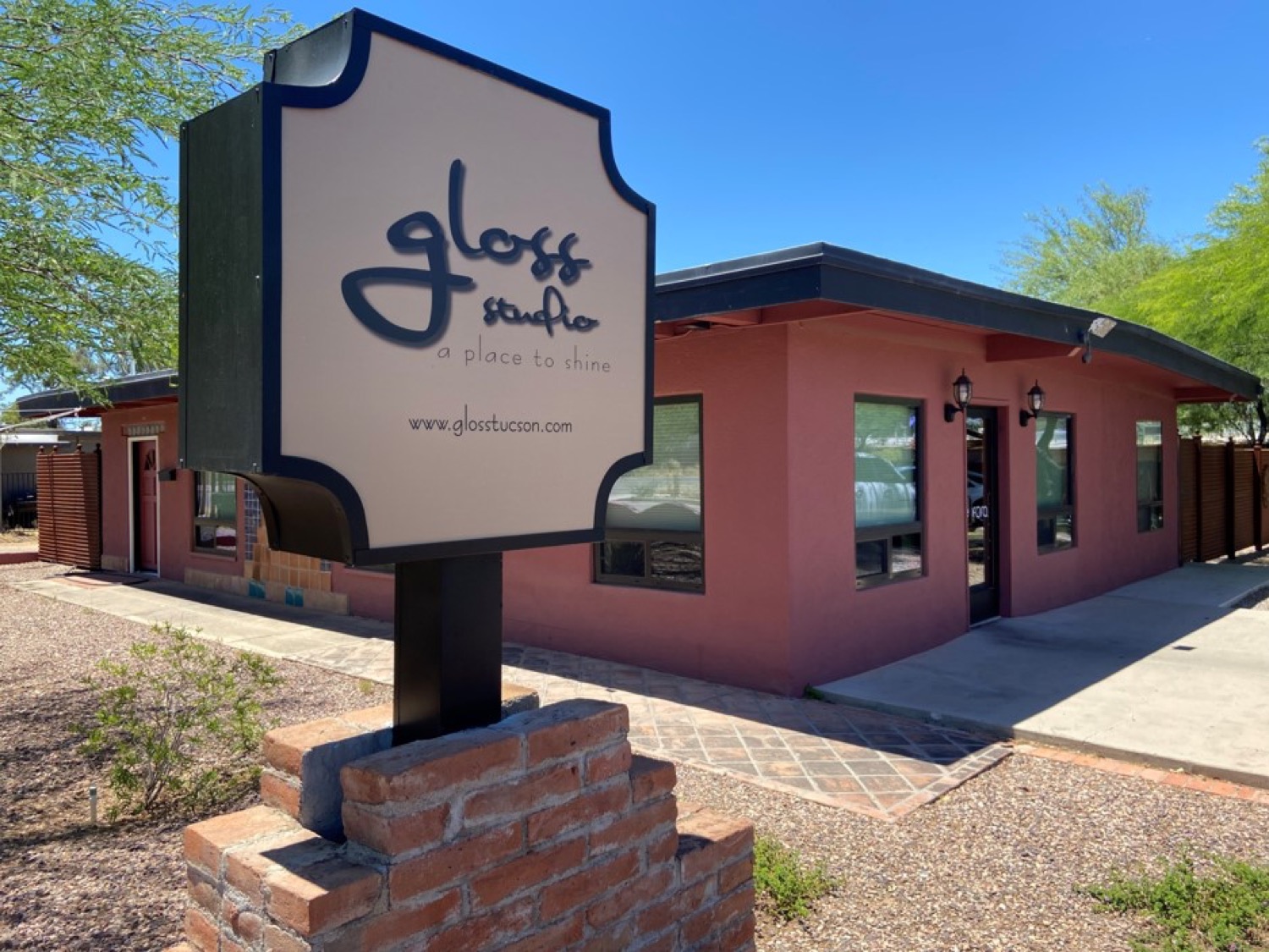The Gloss Studio sign reading “gloss studio, a place to shine” outside the salmon-stucco building on N Sahuara Ave